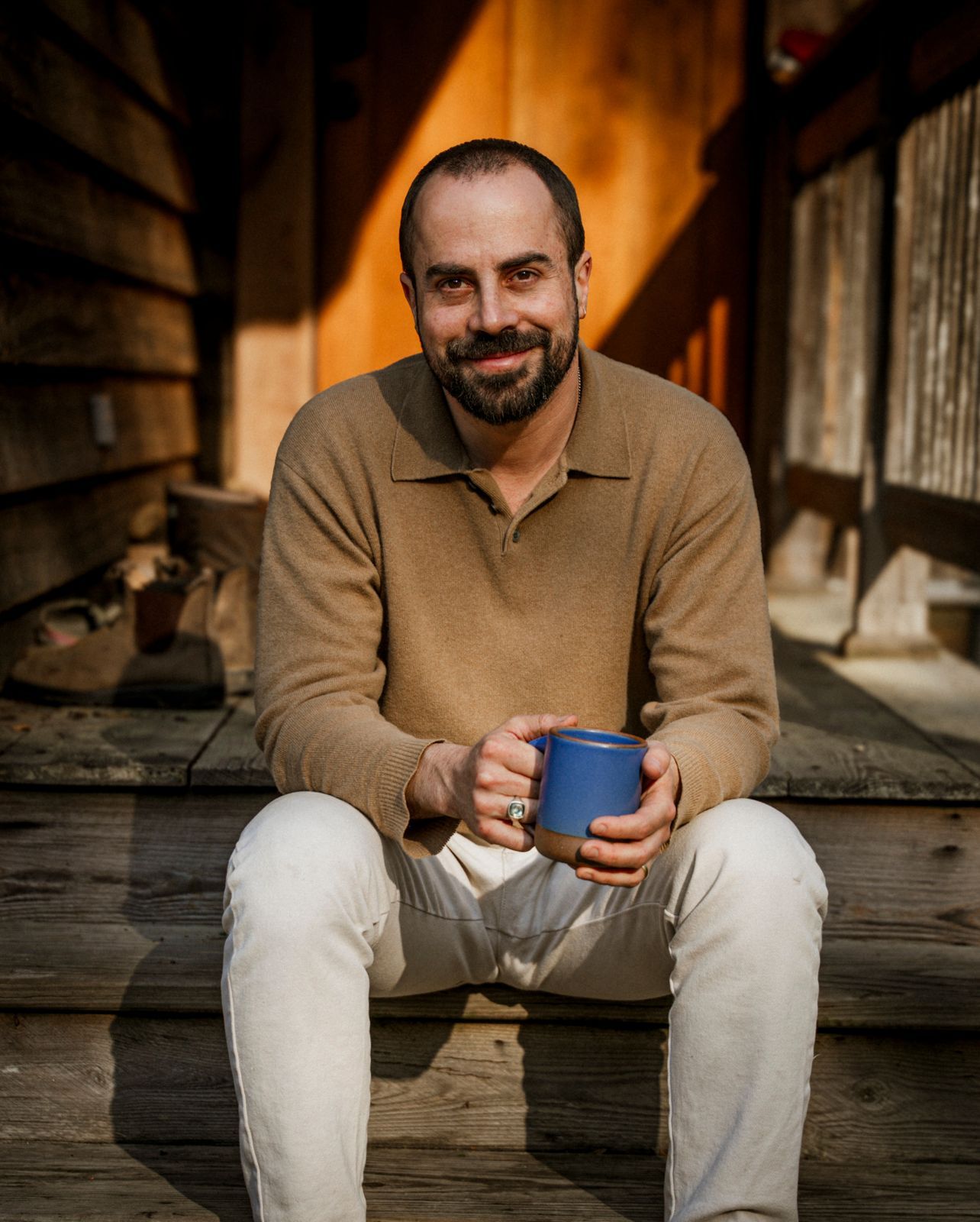 Image may contain Person Sitting Cup Adult Head Face Happy Smile Clothing and Pants