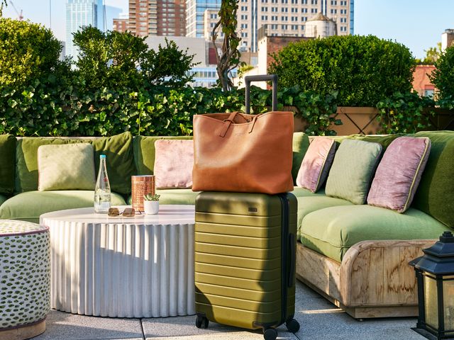 An olive green suitcase with brown leather bag resting on top on a rooftop patio on a sunny day