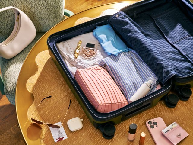 Above view of an open suitcase with various clothing, accessory, and cosmetic products inside and scattered around it