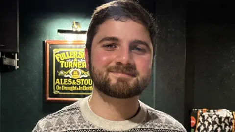 Costa Christou smiling in a Christmas jumper.