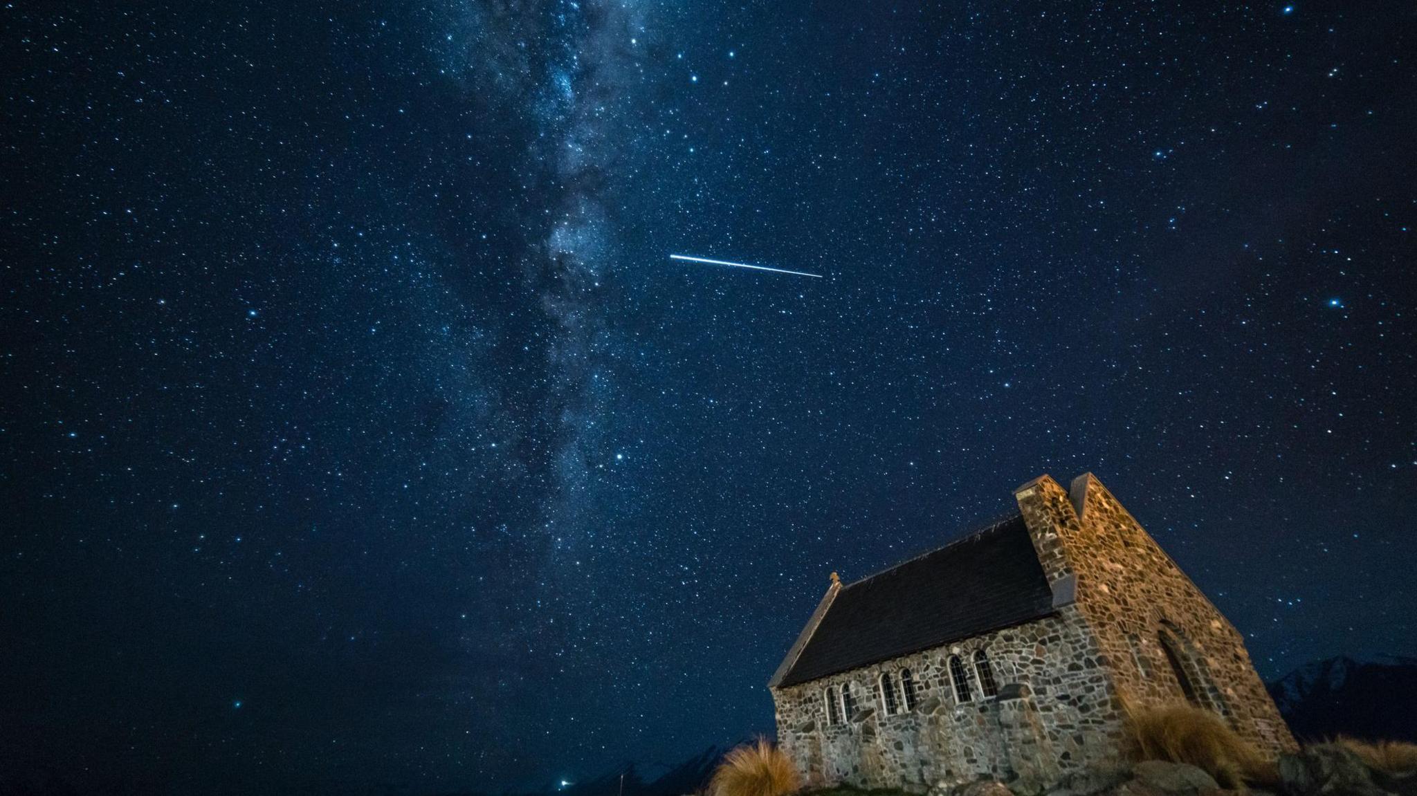 Streak of light in star-filled dark night sky above a church