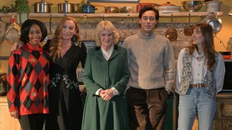 PA Queen Camilla (centre) poses with actors (left to right) Nafessa Williams, Victoria Smurfit, Alex Hassell and Bella Maclean during a visit to the set of the series Rivals in Bristol, to celebrate British television production, youth opportunity in the creative industries, and the legacy of her friend, the author Dame Jilly Cooper.