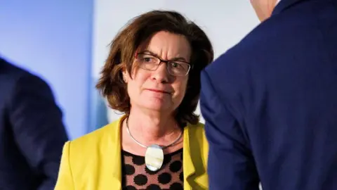 EPA Eluned Morgan, who has short brown hair with glasses and is wearing a yellow jacket