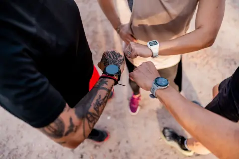 Getty Images Three runners look at their wrists with smartwatches attached, an image taken from above focusing on their arms and wrists.