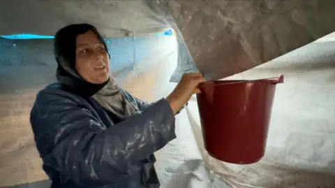 Ghadir al-Adham collects rain from the roof of the family's leaky makeshift shelter