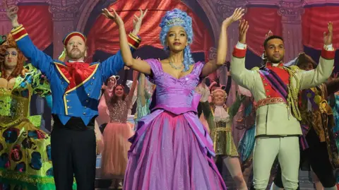 Sky UK Kiefer Sutherland, Savannah Lee Smith, Lucien Laviscount and other cast members in their panto costumes on stage with their arms raised