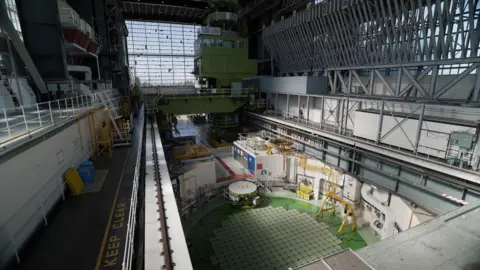 The top of a circular nuclear reactor in the foreground with a turbine hall stretching into the distance.
