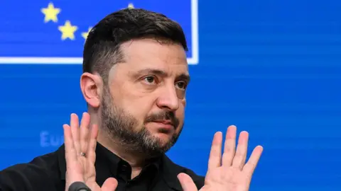 JOHN THYS/AFP Ukraine's President Volodymyr Zelensky gestures as he speaks during a press conference as part of the European Council meeting in Brussels on December 18, 2025