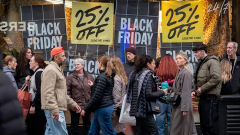 Getty Images A crowd of people dressed in warm clothing walk along Oxford Street in London, in front of a department store advertising discounts in-store for Black Friday