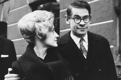 Getty Images Stanley and Moira Baxter outside court in 1962. This is a news photo in black and white and he has his arm around her.