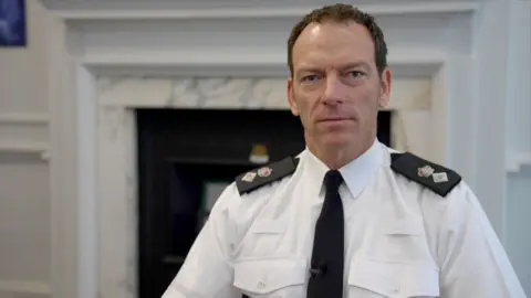 Marc Clothier is sitting in his office, seated in a chair in front of a black and white fire place.
