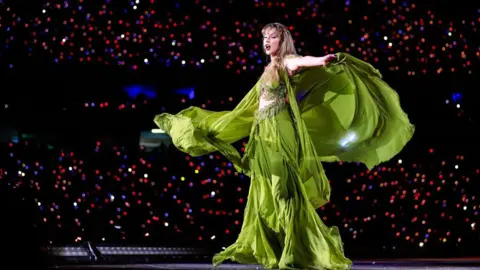 Getty Images Taylor Swift in a flowing green dress during her Eras Tour on stage