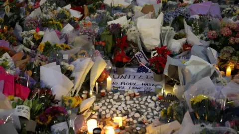Reuters Candles, flowers and pebbles surround a sign that says 'united, no more hate'.