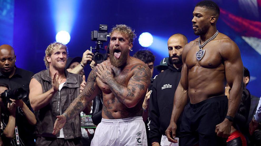 Jake Paul sticks his tongue as Anthony Joshua stares at him during a weigh-in