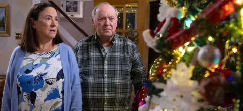 Arabella Weir as Beth and Alex Norton as Eric, pictured with a Christmas tree for the festive episode of Two Doors Down