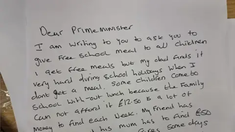 A letter apparently written by a child to Prime Minister Rishi Sunak in 2023. It says, "Dear Prime Minister, I am writing to you to ask you to give free school meals to all children. I get free school meals but my dad finds it very hard during school holidays when I don't get a meal. Some children come to school without lunch because the family cannot afford it. £12.50 is a lot of money to find each week. My friend has ..." and then the text runs out.