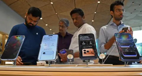 Getty Images Four men see checking models of iPhone 17 series kept on display inside the Apple store at a mall in Mumbai. Two of them are wearing dark blue shirts while one wears a white and another wears a grey shirt.