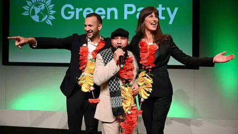 Getty Images Green Party leader Zack Polanski (l), Mothin Ali, Deputy Leader of the Green Party and Rachel Millward, Deputy Leader of the Green Party react to the crowd after both of the deputy leader speeches on the second day of the Green Party Conference