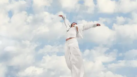 Pantone Person wearing all white in front of a backdrop of sky and clouds