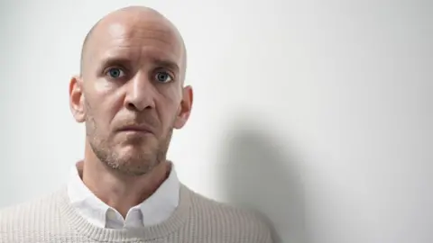 PA Media Daniel Barr is wearing a beige jumper with a white shirt and is staring directly at the camera.