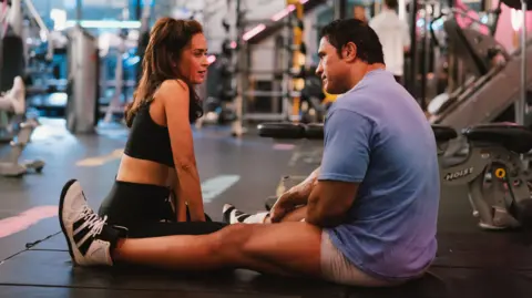 A24 Emily Blunt and Dwayne Johnson, sitting on the floor of a gym, in The Smashing Machine