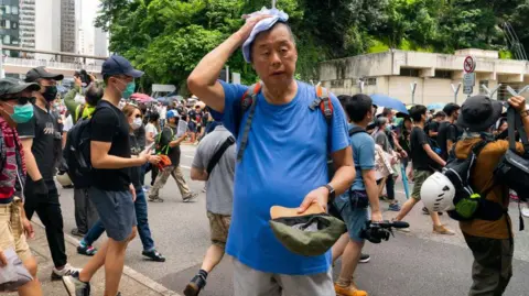 Getty Images Jimmy Lai, in a blue tee, was putting a towel over his head during a pro-democracy march on 31 Aug 2019. Behind him were dozens of other protesters, many of them wearing surgical masks.