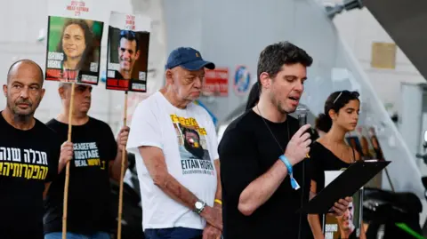 Reuters Gil Dickmann (2nd Right), cousin of dead hostage Carmel Gat, speaks at a rally demanding the release of all the hostages in Gaza, in Tel Aviv, Israel (4 October 2025)
