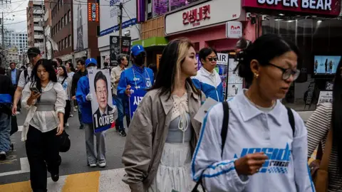 Getty Images Supporters of Lee Jae-myung, dressed in blue outfits, hold placards in a shopping district
