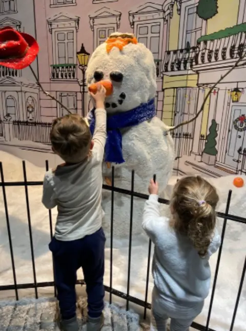 George Lewis Two children looking away from the camera touching a snowman