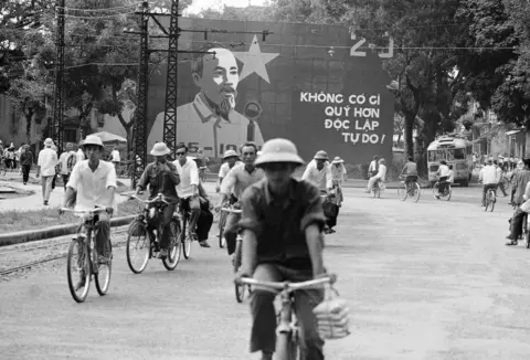 AP Photo/Peter Arnett/File North Vietnamese bicycle through the streets of Hanoi, past a bulletin board with a Ho Chi Minh, Oct. 2, 1972.