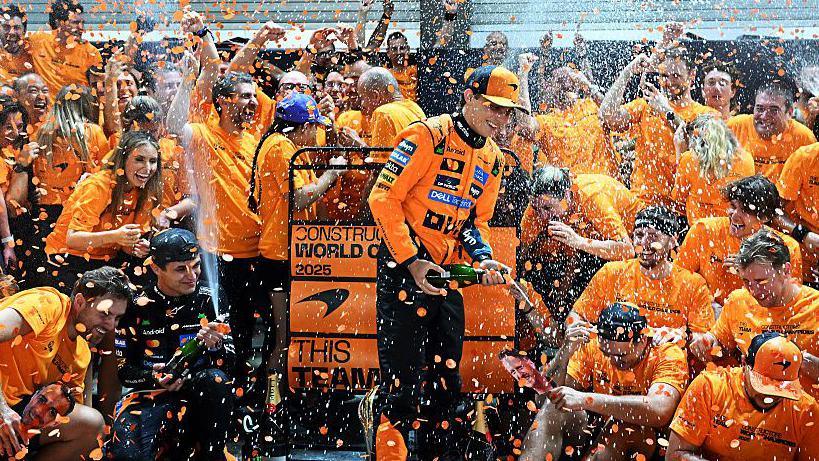 McLaren team members celebrating winning the constructors' championship after the Singapore Grand Prix, as drivers Lando Norris and Oscar Piastri spray champagne