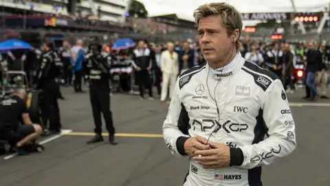 Warner Bros Brad Pitt in F1, standing on a race track