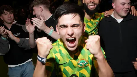 Baller League/Cameron Fillery Bryan Ly wears a green and yellow Yanited jersey. He has his fists raised and clinched and is shouting into the camera.
