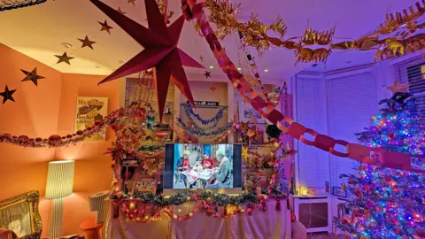 Felicity Hayward A living room with 80s era decorations, paper chains, tinsel and metallic garlands