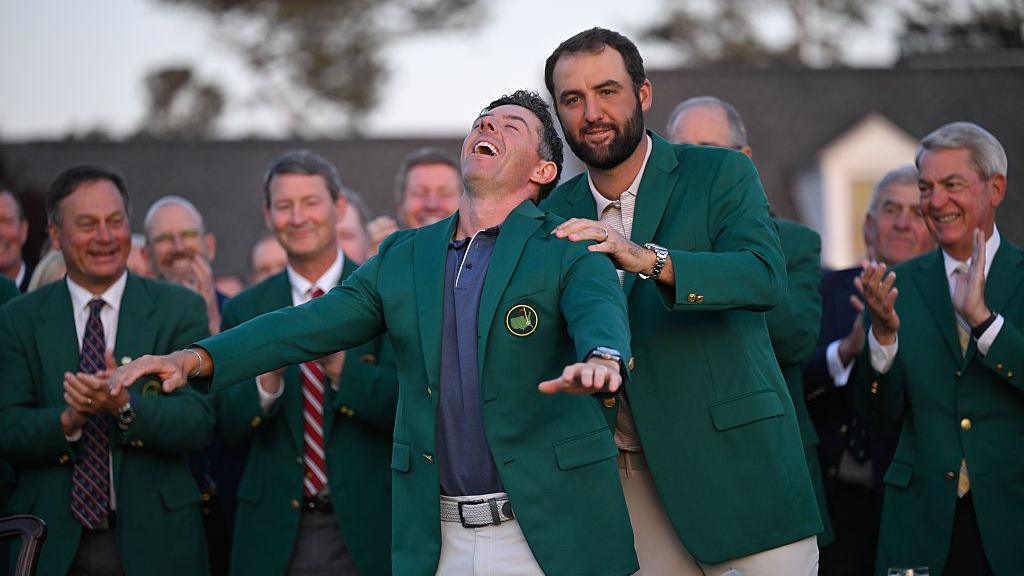 Rory McIlroy of Northern Ireland is awarded the green jacket by Scottie Scheffler
