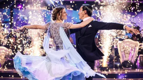 Karen Carney and Carlos Gu performing against a glittery background on Strictly