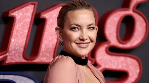 Cindy Ord/WireImage Kate Hudson, with her hair tied back, smiling for the camera at some sort of premiere/red carpet event